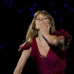 a woman in a red dress covers her mouth with her hands as she sings on stage