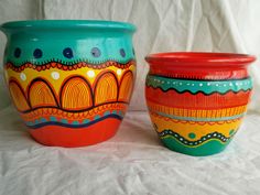 two colorful pots sitting next to each other on a white sheeted surface, one has an orange rim and the other is green