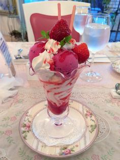 an ice cream sundae with strawberries and whipped cream in a glass on a table