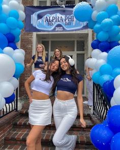 three girls posing in front of a building with blue and white balloons