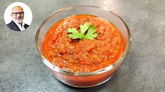 a glass bowl filled with red sauce and garnished with cilantro leaves