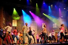 a group of people standing on top of a stage next to each other in front of bright colored lights