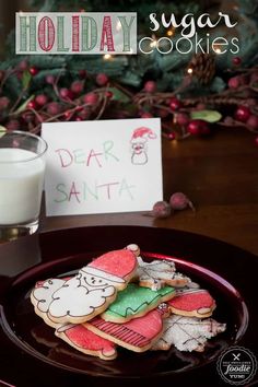 some cookies are on a plate next to a glass of milk and a sign that says holiday sugar cookies