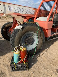 an orange truck parked on top of a sandy beach next to a blue bucket filled with gas cans