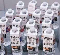 many bottled water bottles sitting on top of a glass table with labels reading wanna buy a house?