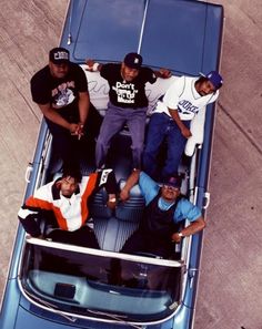 four men sitting in the back of a blue car with their arms around each other