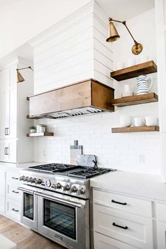 a stove top oven sitting inside of a kitchen next to white cabinets and wooden shelves