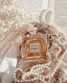 a chanel bottle sitting on top of a book next to some pearls and flowers