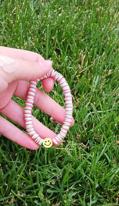 a hand holding a ring with a smiley face on it in the middle of some grass