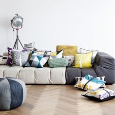 a living room filled with lots of pillows on top of a wooden floor next to a white wall