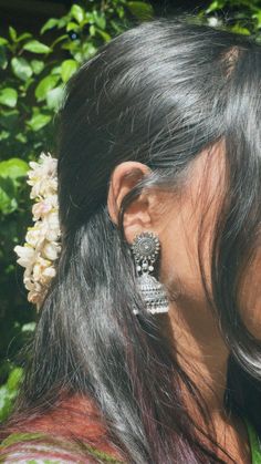 a close up of a person wearing ear rings and flowers in her hair with trees behind them