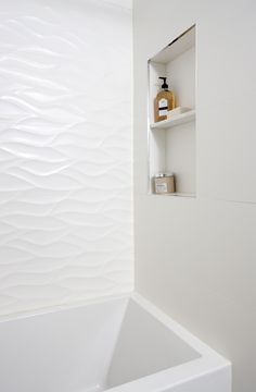 a white bath tub sitting next to a bathroom wall with shelves on the opposite side