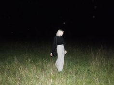 a woman standing in the middle of a field at night with her head turned to the side