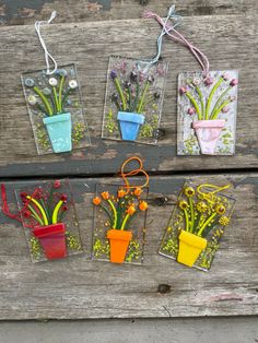 four flower vases with flowers in them on a wooden surface, hanging from strings