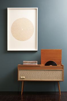 a record player sitting on top of a wooden dresser next to a framed art piece