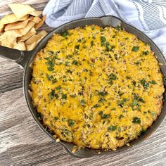 a casserole with cheese and herbs in a cast iron skillet next to chips