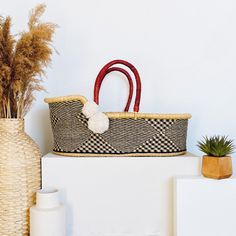 a basket sitting on top of a white shelf next to a vase with plants in it