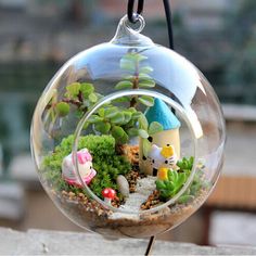 a glass ball filled with plants and small figures in the center is hanging from a black cord