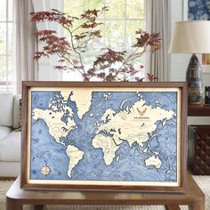 a framed world map sitting on top of a wooden table in front of a window