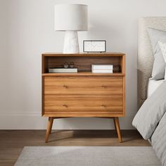 a bedroom with a bed, nightstand and lamp on the night stand in front of it