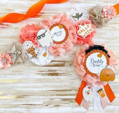 two paper flowers with halloween stickers on them sitting next to orange ribbons and an orange bow