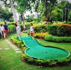 people are standing around an artificial miniature golf course in the park, while one person takes a photo