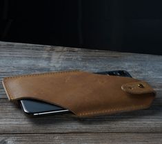 a cell phone in a leather case on a wooden table next to an open wallet