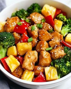 a white bowl filled with broccoli, pineapple and tofu stir fry