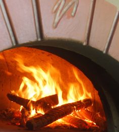 a wood fired oven with fire burning in it's side and flames on the inside