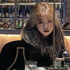 a woman sitting at a table with glasses in front of her and bottles behind her