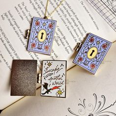 two square pendants sitting on top of an open book next to a key lock