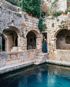 a woman standing in an old stone building next to a pool filled with blue water