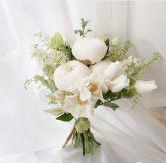 a bridal bouquet with white flowers and greenery on the bottom is sitting in front of a curtain