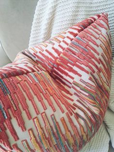 an orange and red pillow sitting on top of a white couch next to a blanket