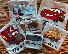 four t - shirts with cars and trucks on them sitting on a wooden table next to each other