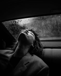 a woman sleeping in the back seat of a car with rain falling down on her head