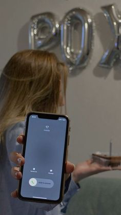 a woman holding an iphone in front of a wall with the number seventy on it