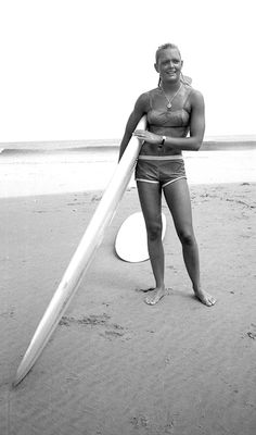 a woman standing on the beach holding a surfboard in front of her face and smiling