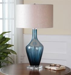 a blue vase sitting on top of a table next to a lamp and a book