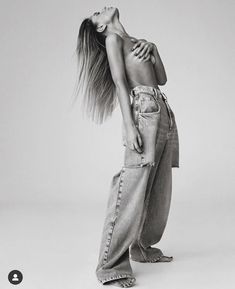 a black and white photo of a woman with her hair blowing in the wind wearing jeans