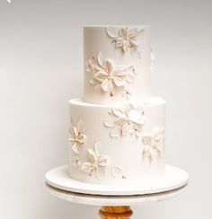 a three tiered white wedding cake with flowers on the top and bottom, sitting on a wooden stand