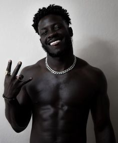 a man with no shirt holding two fingers up to the side and wearing a chain around his neck