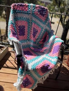 a crocheted blanket sitting on top of a wooden deck next to a chair