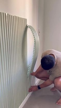 a man kneeling on the ground next to a wall with a curved metal strip attached to it