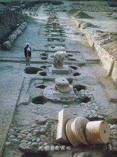 there is a man walking down the street next to some ancient ruins and vases