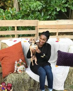 a woman sitting on a couch holding a small dog in her lap and smiling at the camera