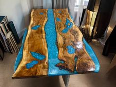 a table made out of wood with blue paint on the top and bottom, sitting in front of a window