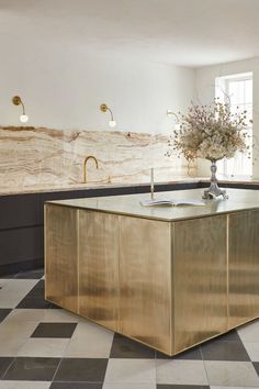 a kitchen with black and white checkered flooring, gold cabinetry and marble counter tops