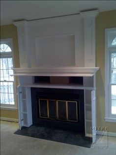 an empty living room with a fireplace and two windows in the wall above it is painted white