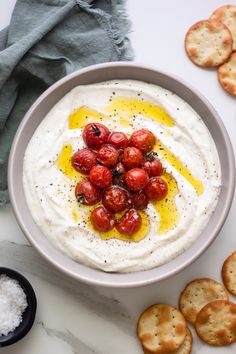 a bowl of dip with crackers and cherry tomatoes on the side next to it